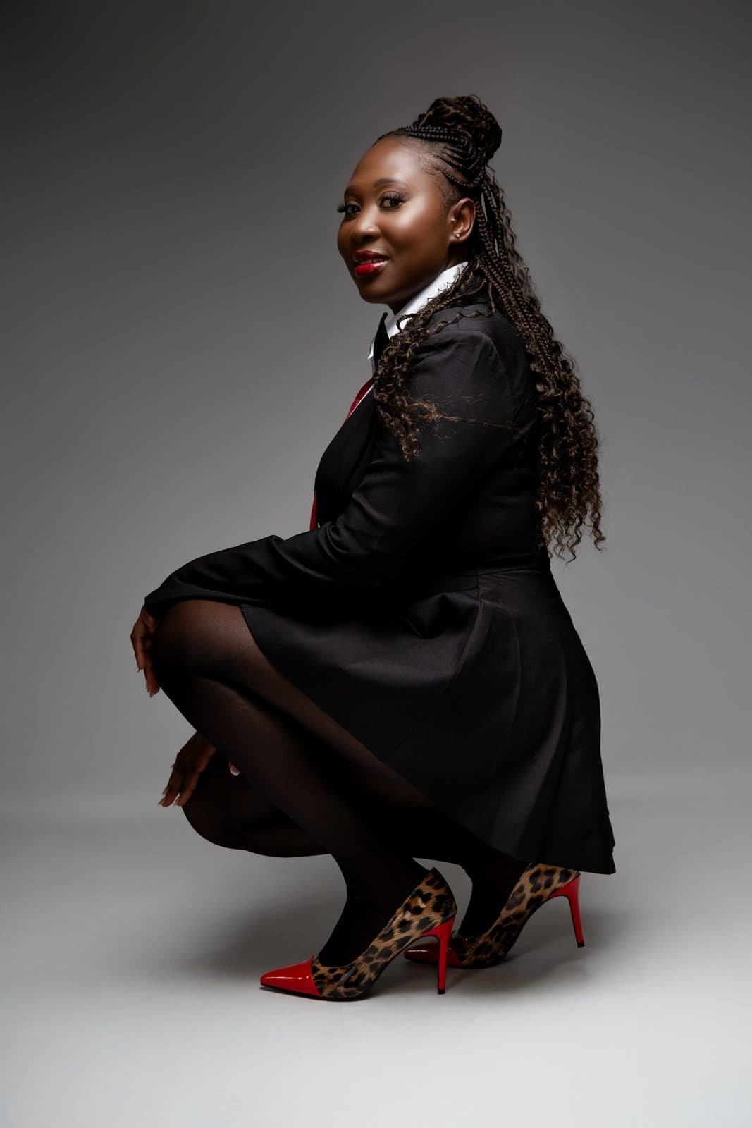 Woman in black suit and red tie crouching in studio portrait